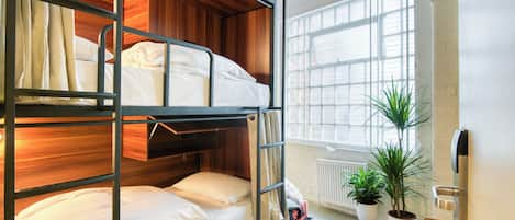 Une chambre avec un lit superposé, une tête de lit en bois, du linge de lit blanc, un radiateur et des plantes en pot.