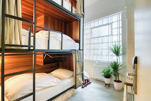 Une chambre avec un lit superposé, une tête de lit en bois, du linge de lit blanc, un radiateur et des plantes en pot.