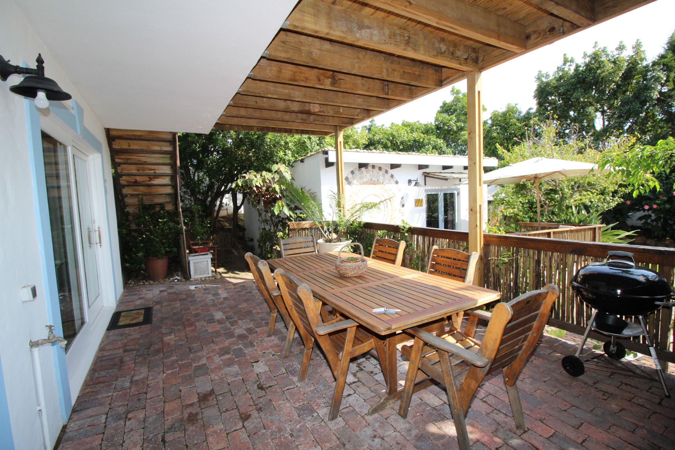 Eine Terrasse mit Holztisch und -stühlen, einem Grill und einem überdachten Bereich mit Holzboden.