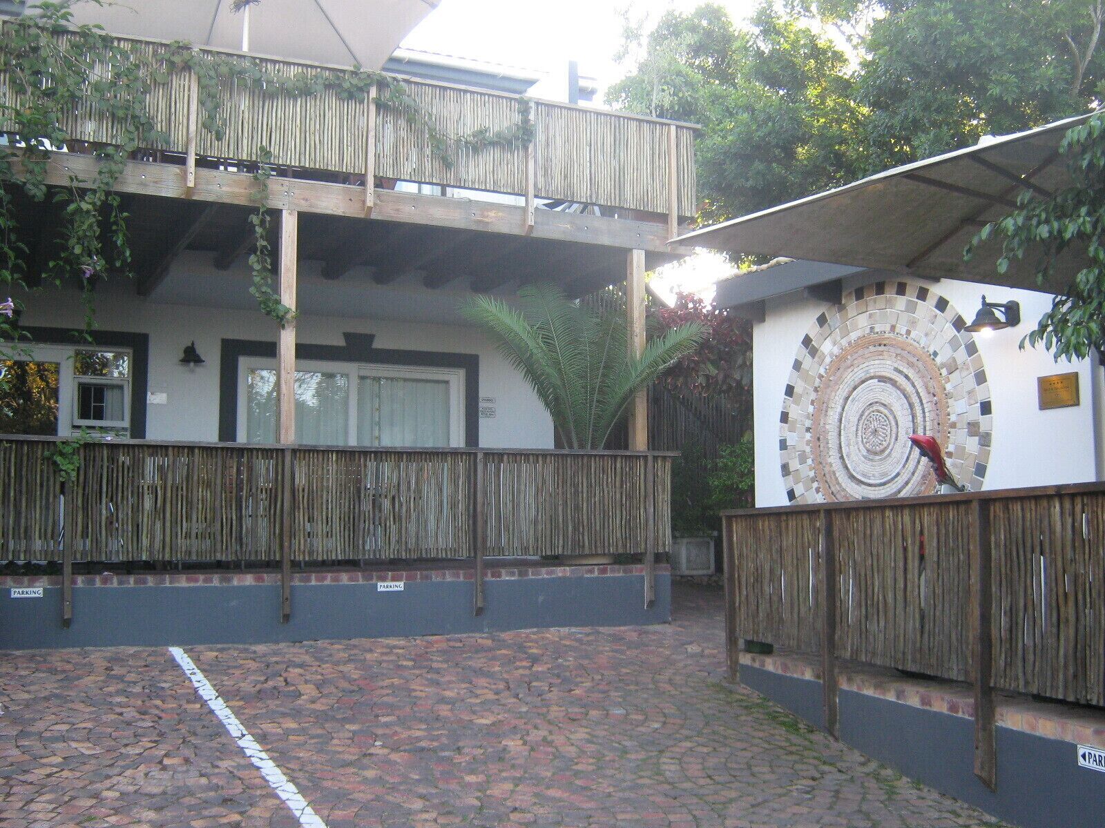 A building with a wooden balcony, a tiled wall with a circular mosaic, and a paved courtyard.