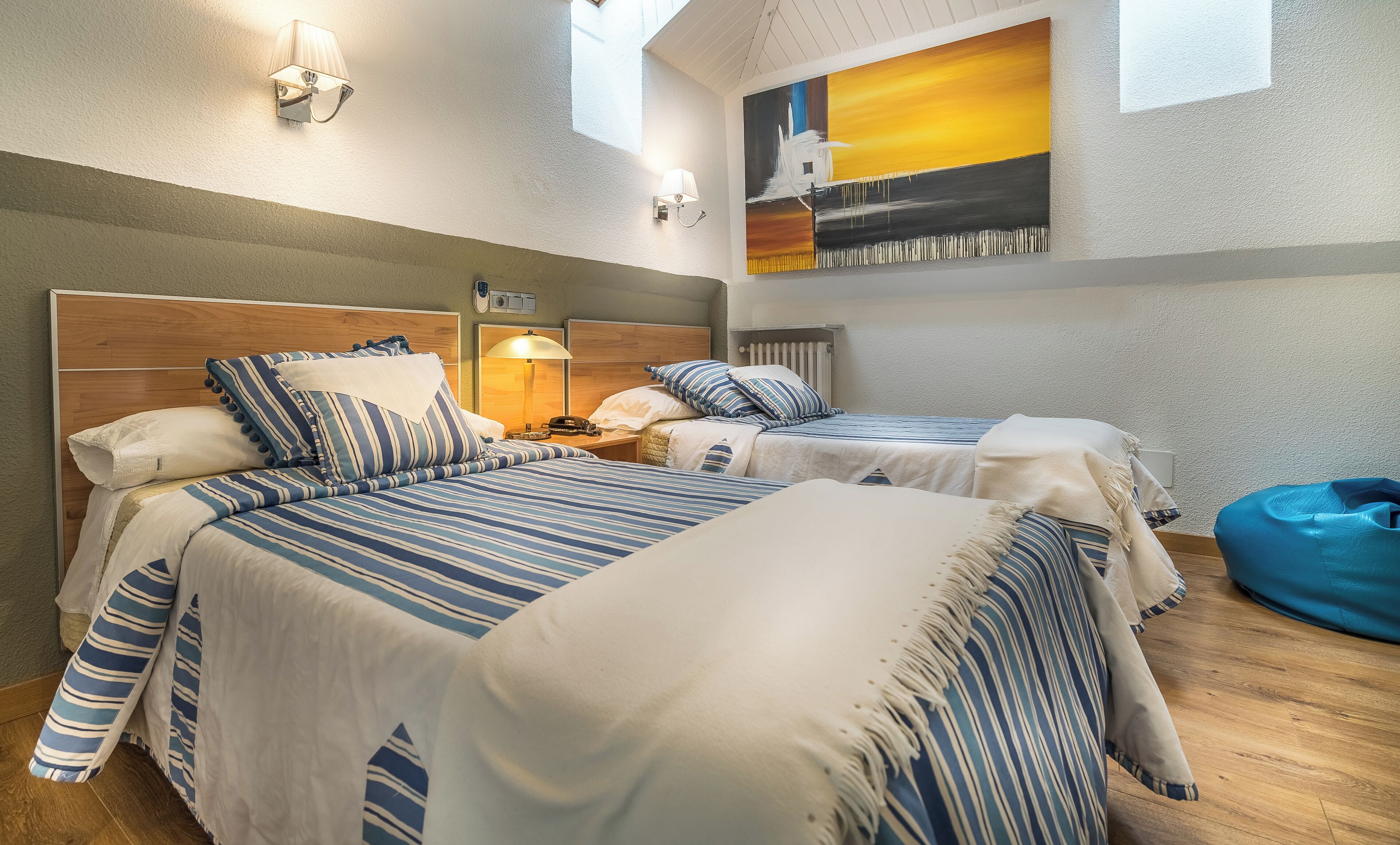 Une chambre d’hôtel avec deux lits, une literie à rayures, une table de chevet avec une lampe et un tableau au mur.