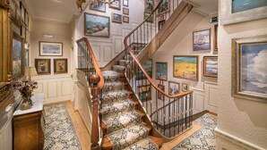 A grand staircase with ornate railings and patterned carpet, surrounded by framed artwork and a chandelier. - Hotel Boutique Las Brisas (Santander)