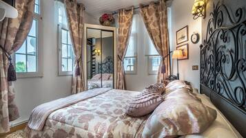 Un dormitorio con una cama grande, cortinas florales, un espejo y lámparas fijadas a la pared.