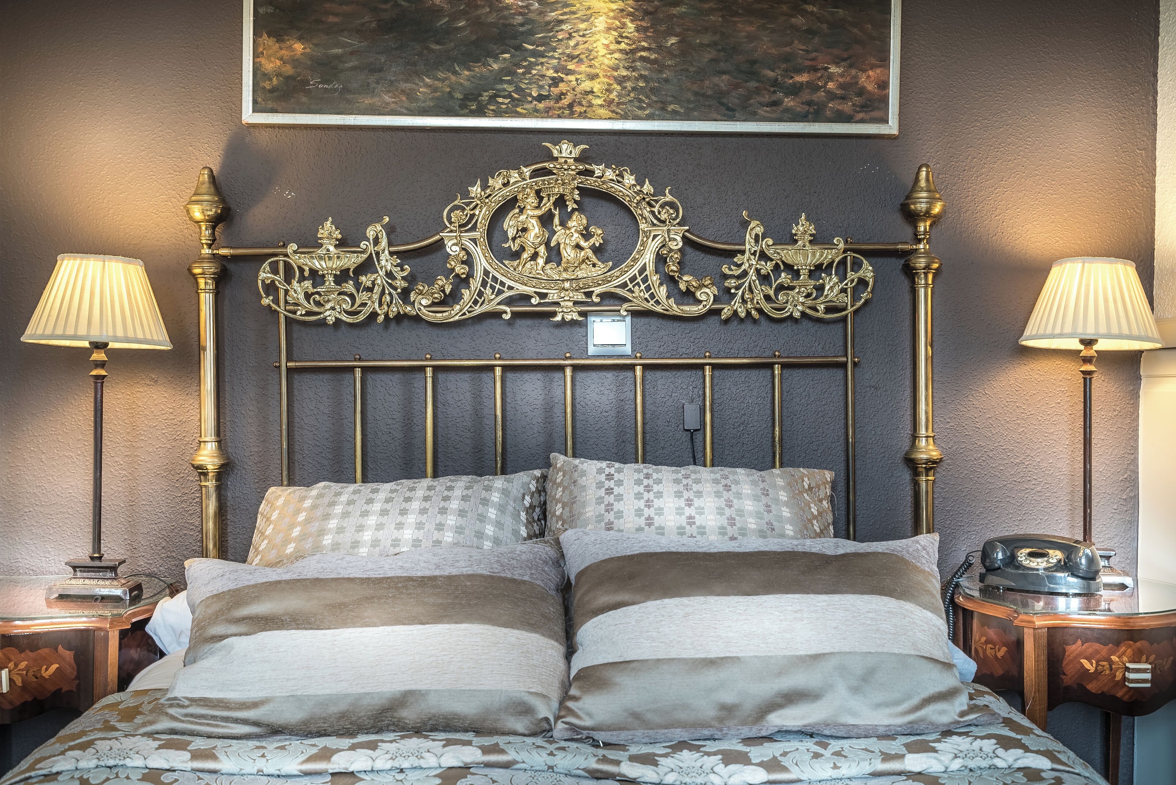A bed with ornate headboard, two bedside lamps, and a vintage telephone on a nightstand.