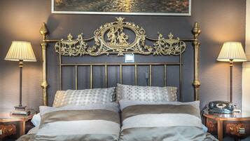 Una cama con una cabecera ornamentada, dos lámparas de noche y un teléfono antiguo sobre una mesita de noche.
