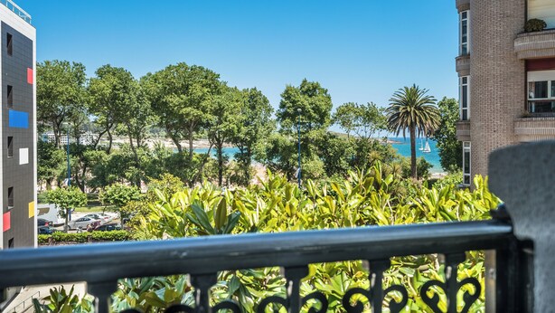A balcony with a view of a beach, palm trees, and a parking lot. - Hotel Boutique Las Brisas (Santander)