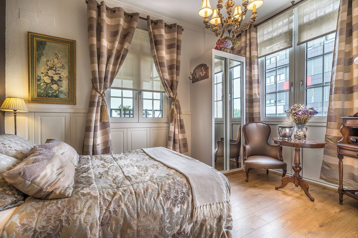 A bedroom with a large bed, a chandelier, a chair, and a table with flowers.