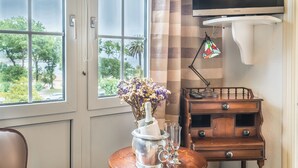 A room with a large window, a wooden table with a metal pitcher and glasses, a wooden cabinet, and a TV mounted on the wall. - Hotel Boutique Las Brisas (Santander)