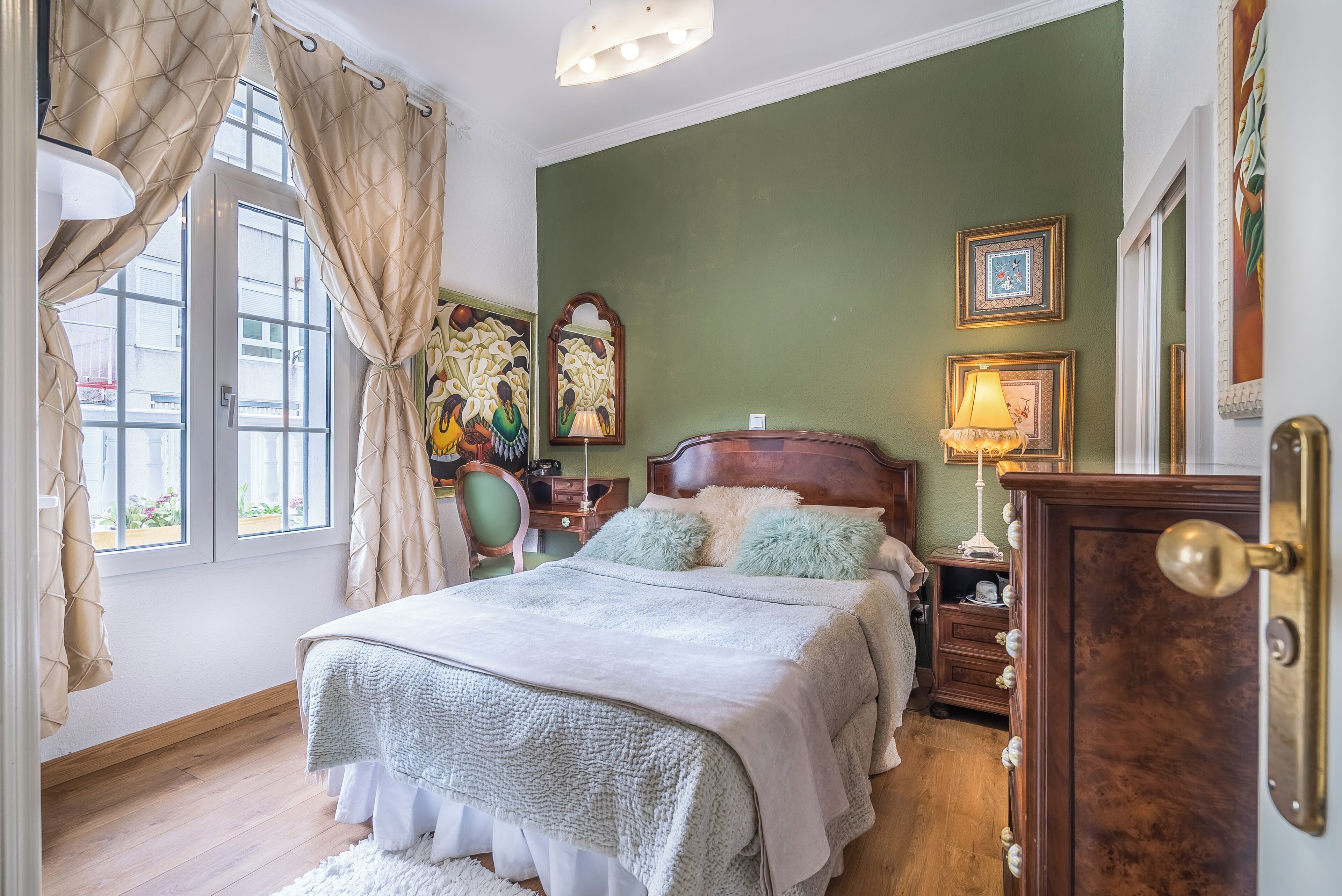 A bedroom with a bed, curtains, a nightstand, a lamp, and wall art.