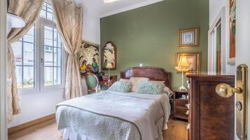 A bedroom with a bed, curtains, a nightstand, a lamp, and wall art.