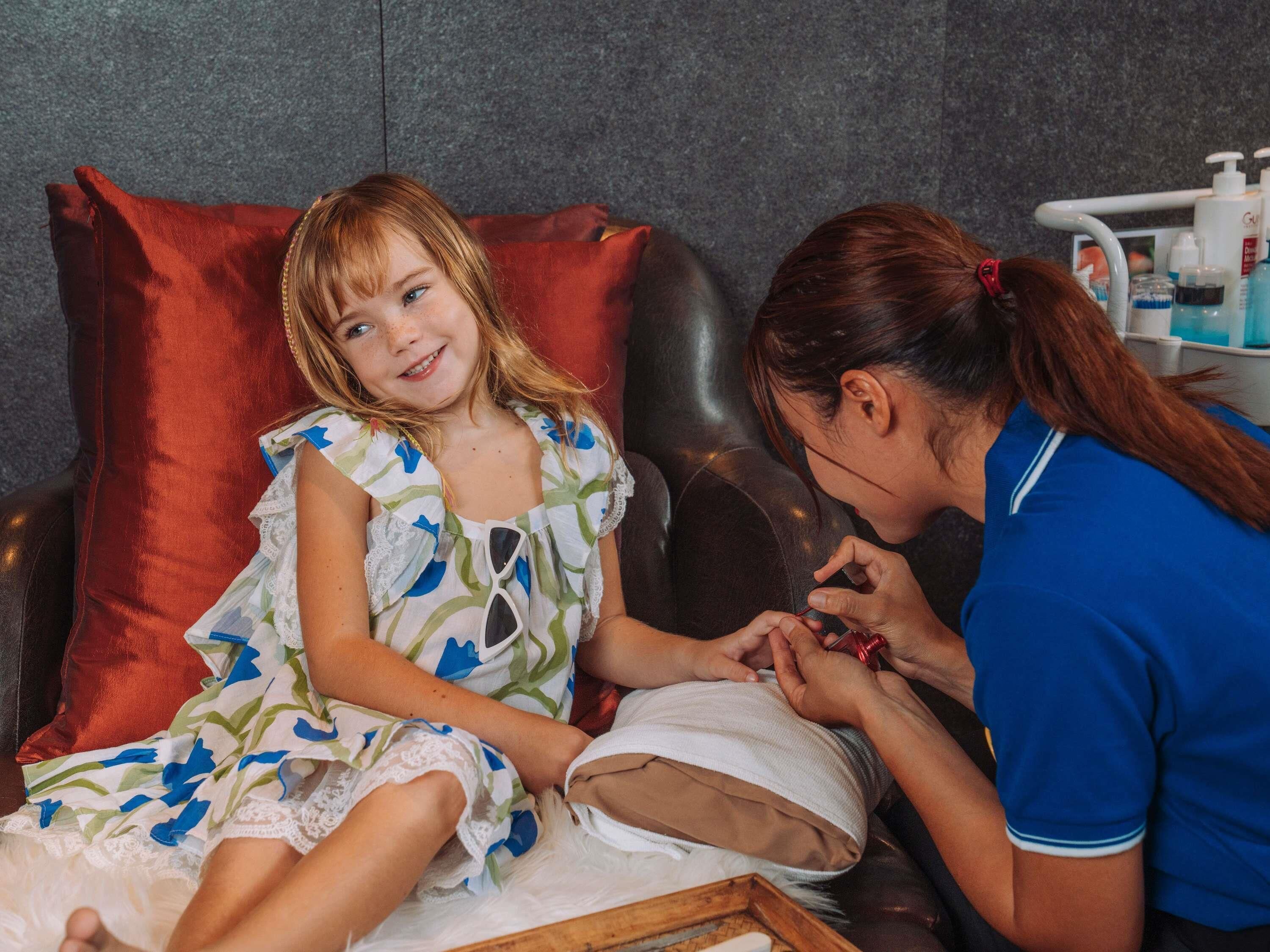 Un enfant et un adulte se trouvent dans une pièce où il y a un fauteuil de massage, un mur blanc et une étagère avec des bouteilles.