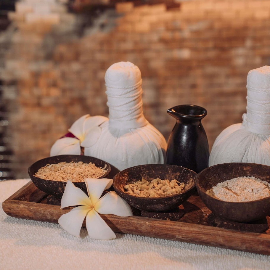 A wooden tray with massage stones, a black stone, and a white flower.