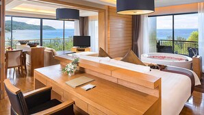 Ein modernes Hotelzimmer mit einer großen Couch, einem Essbereich, einem Fernseher und Blick aufs Meer.