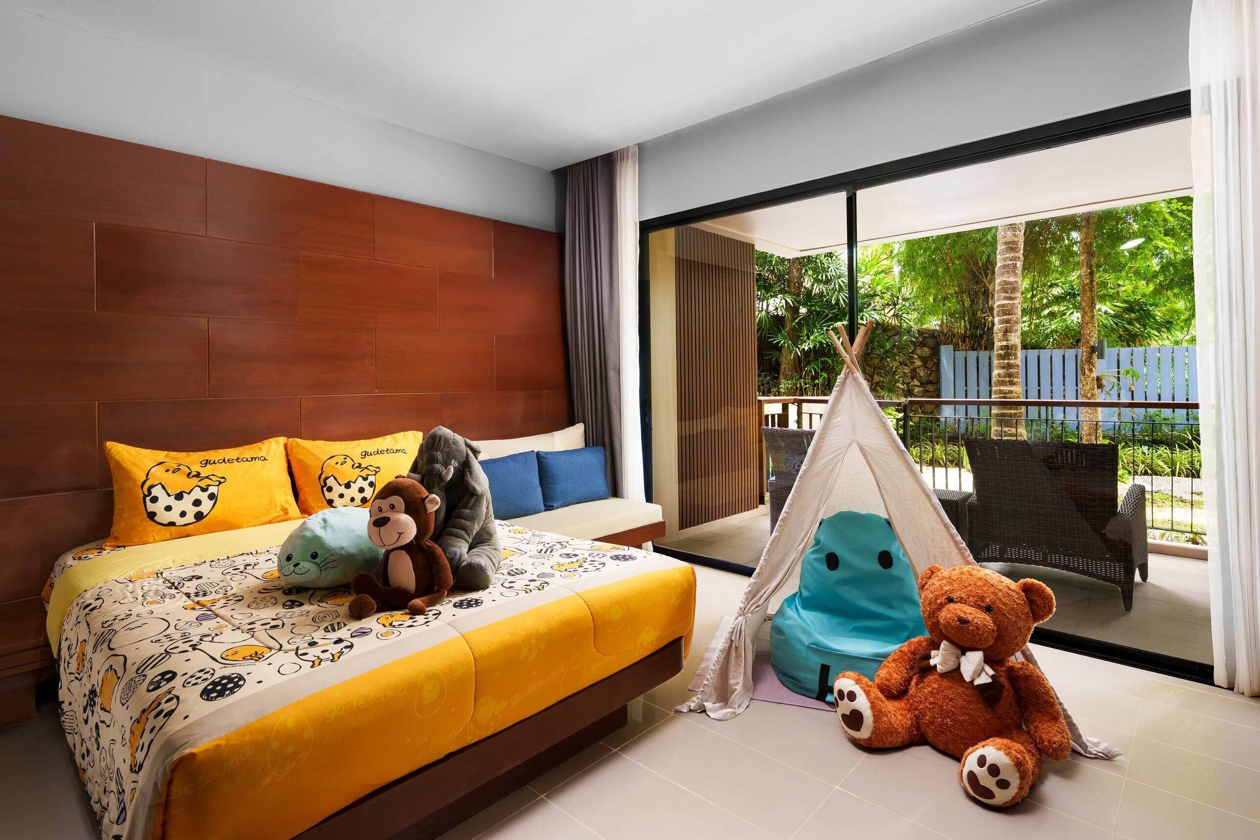 A bedroom with a bed, pillows, stuffed animals, a tent, and a view of greenery outside.