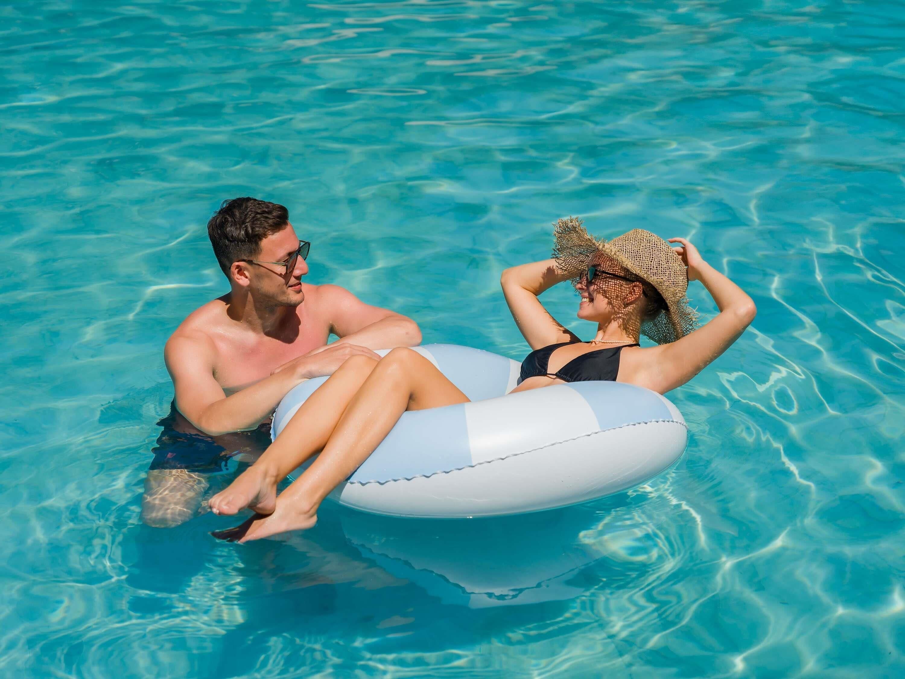Ein Paar im Pool, mit einem aufblasbaren Ring, klares blaues Wasser, ohne sichtbare Einrichtungen oder Architektur.