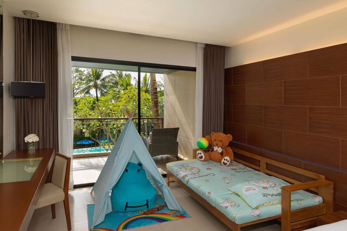Een hotelkamer met een bed, een bureau, een stoel, een kleine speeltent en een teddybeer.