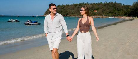 Escena de playa con una pareja caminando sobre la arena, tomados de la mano.