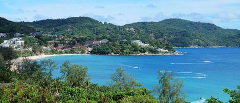 A coastal town with a beach, clear blue sea, and lush green hills.