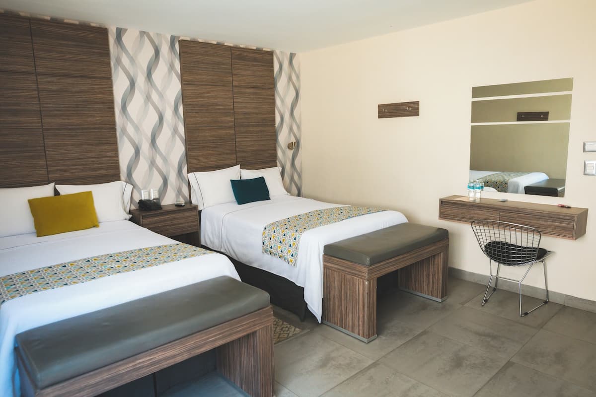 Habitación de hotel con dos camas, un banco de madera, un escritorio con silla y un espejo.