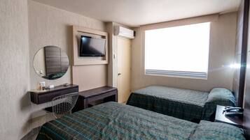 A hotel room with two beds, a desk with a chair, a television, and a window providing natural light.
