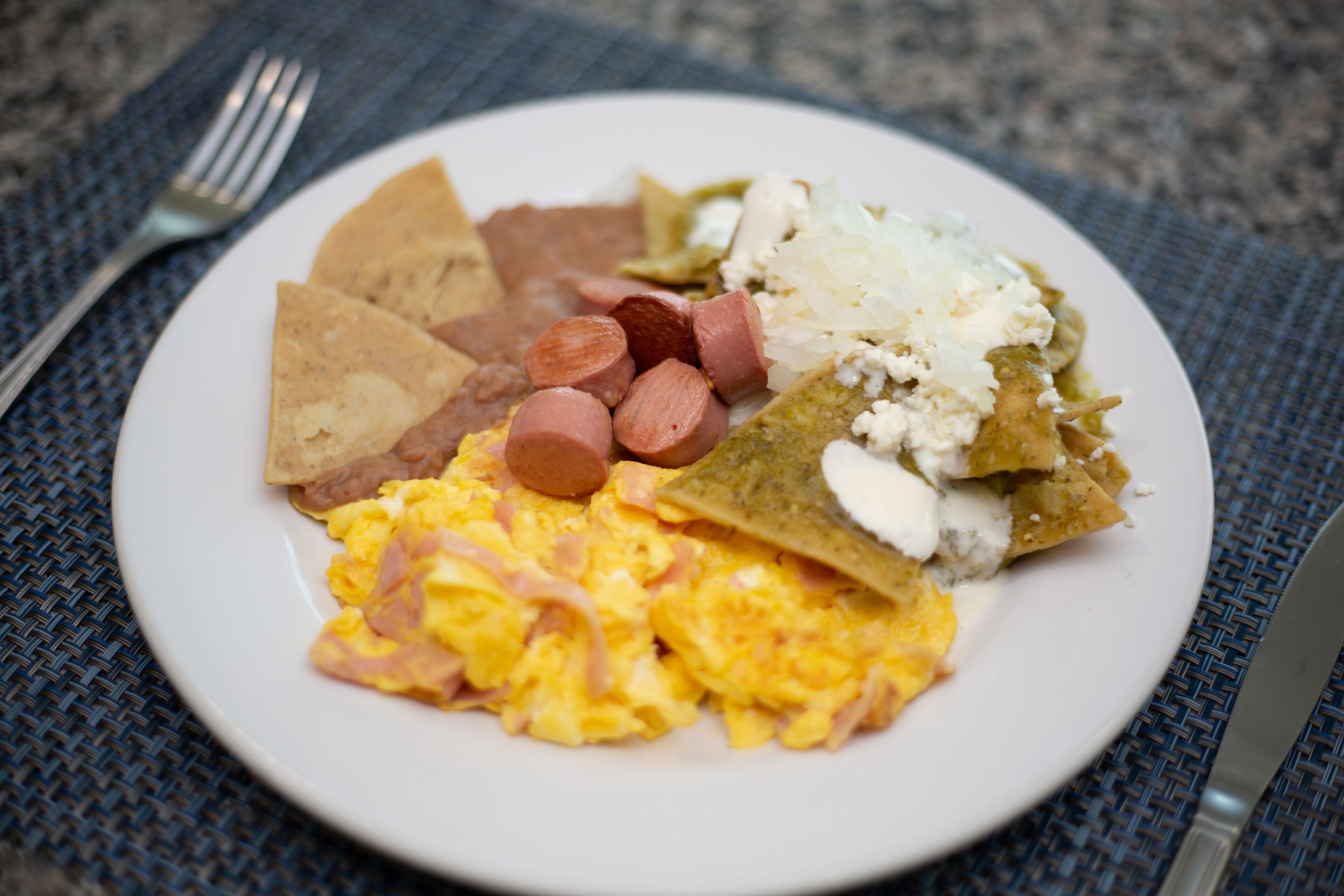A plate of food with scrambled eggs, sausage, and a tortilla dish.