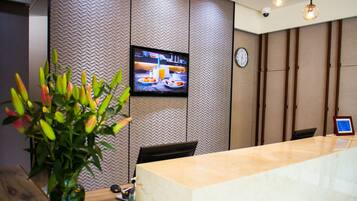 A reception area with a marble counter, a television mounted on the wall, a clock, and a potted plant.