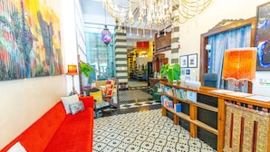 A hotel lobby with a red sofa, a wooden reception desk, a chandelier, and a colorful abstract painting. - CasaBlanca Hotel (San Juan)