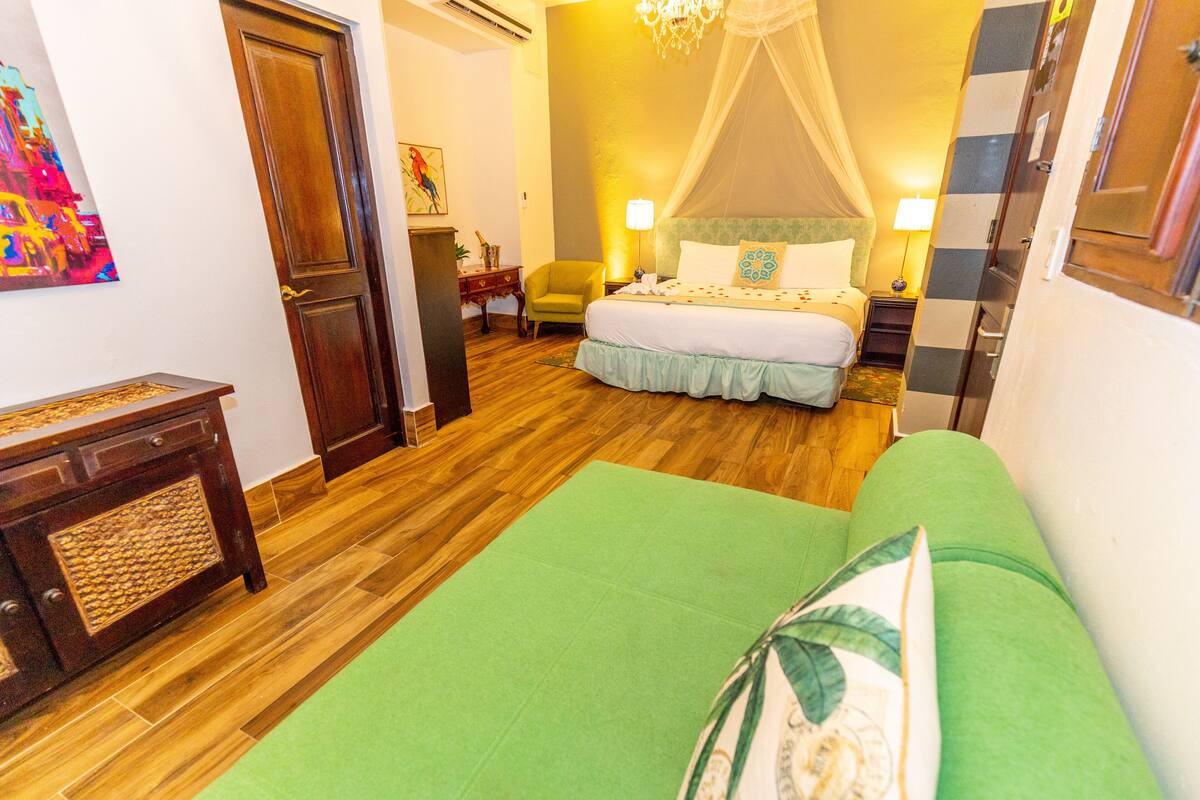 Ein Hotelzimmer mit einem Bett, einem grünen Sofa, einer Holzkommode und einem Sessel.
