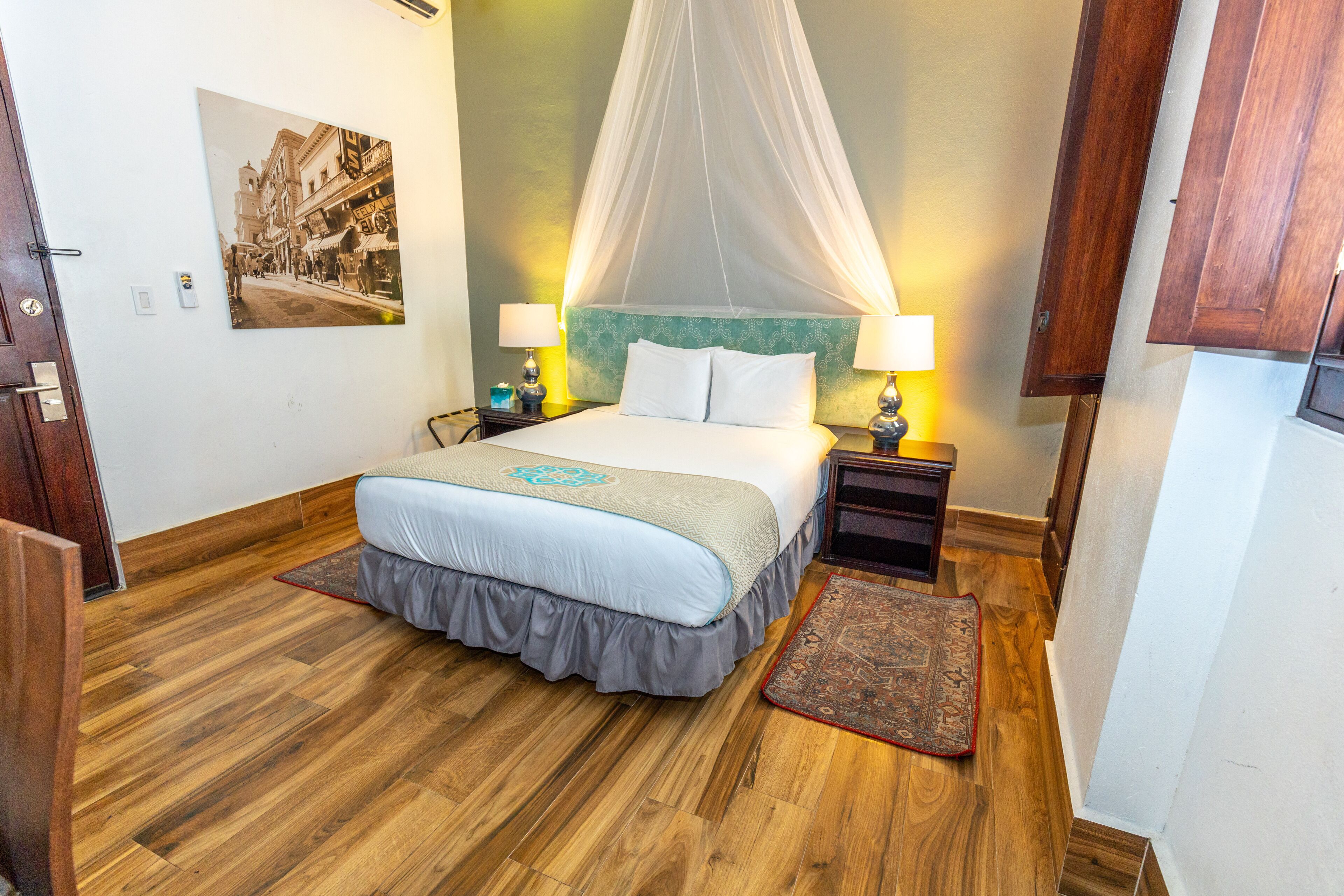 Une chambre à coucher bien rangée, avec un lit, des lampes de chevet, un tapis décoratif et un tableau accroché au mur.