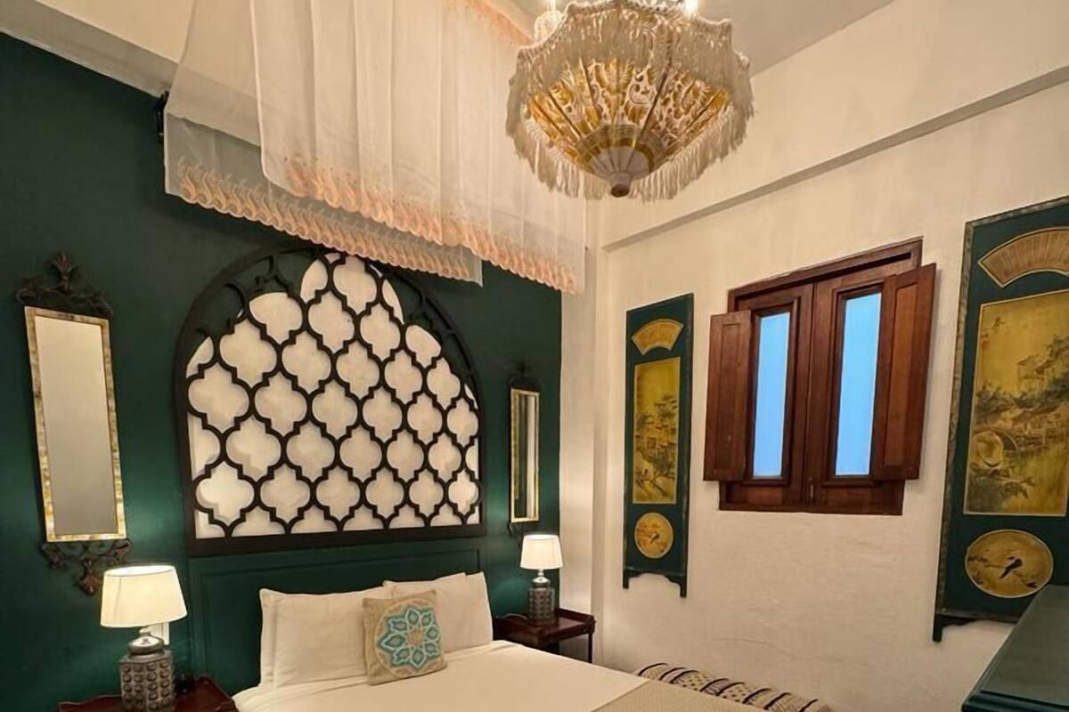 Ein Schlafzimmer mit einem großen Bett, einer Kandelaber, einer Wandverkleidung, einem Spiegel und einer Uhr.