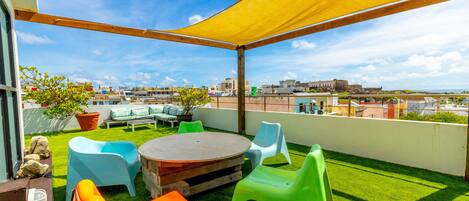 A rooftop terrace with a round table, colorful plastic chairs, and a yellow canopy.