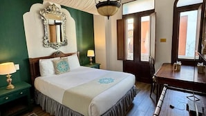 A bedroom with a large bed, a wooden desk, a mirror, and a hanging light fixture. - CasaBlanca Hotel (San Juan)