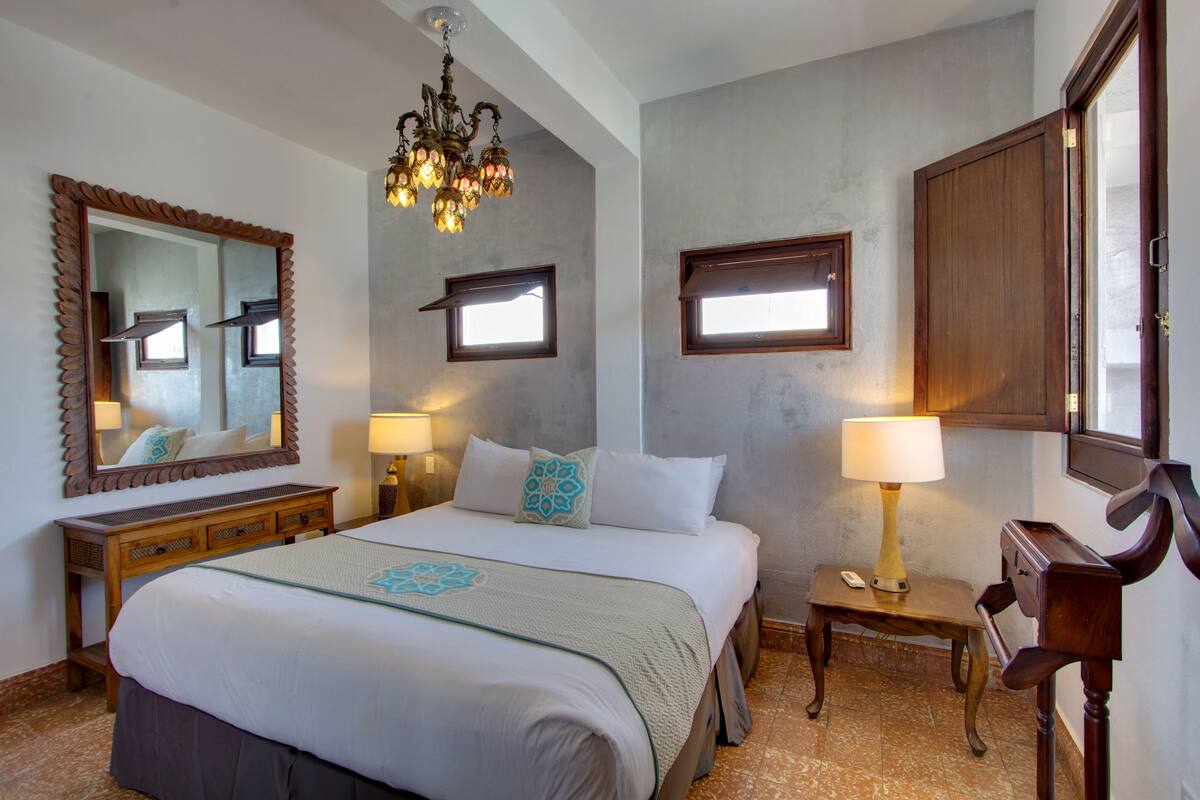 Ein Hotelzimmer mit einem großen Bett, zwei Nachttischen, einer Chandelüster, einem Spiegel und einem Kleiderschrank.