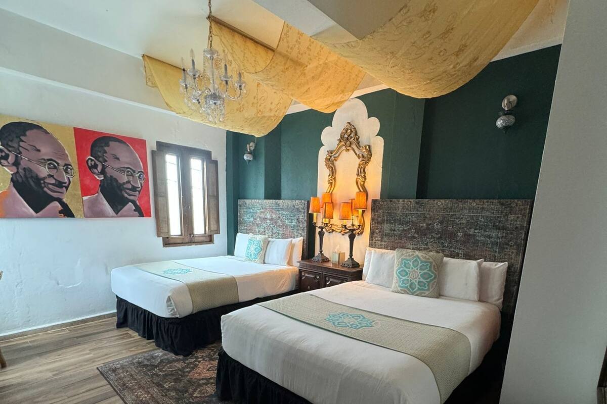 Ein Schlafzimmer mit zwei Betten, einer Kandelaber, einem großen Spiegel und Kunstwerken an den Wänden.