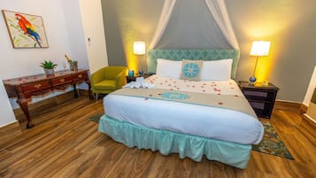 Un dormitorio con cama con dosel, suelo de madera, una mesita de noche con lámpara, una silla, un escritorio con planta y un cuadro en la pared.