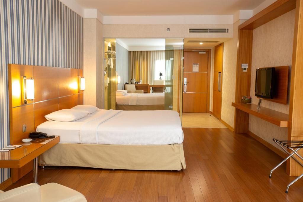 A hotel room with a bed, bedside table, lamp, TV, and a mirror.