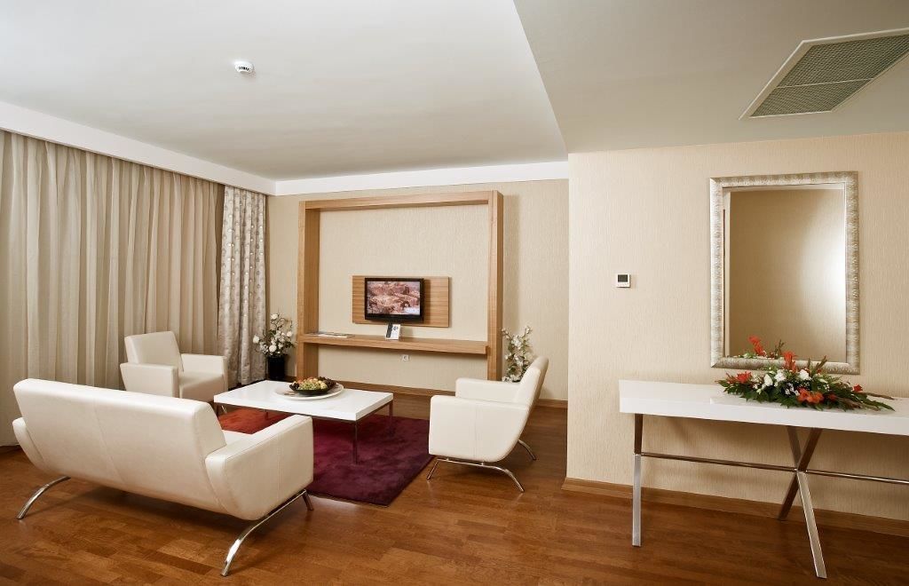 Una sala de estar moderna con un televisor de pantalla plana, muebles blancos, una mesa de centro de madera y un espejo decorativo.