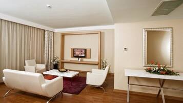 Una sala de estar moderna con un televisor de pantalla plana, muebles blancos, una mesa de centro de madera y un espejo decorativo.