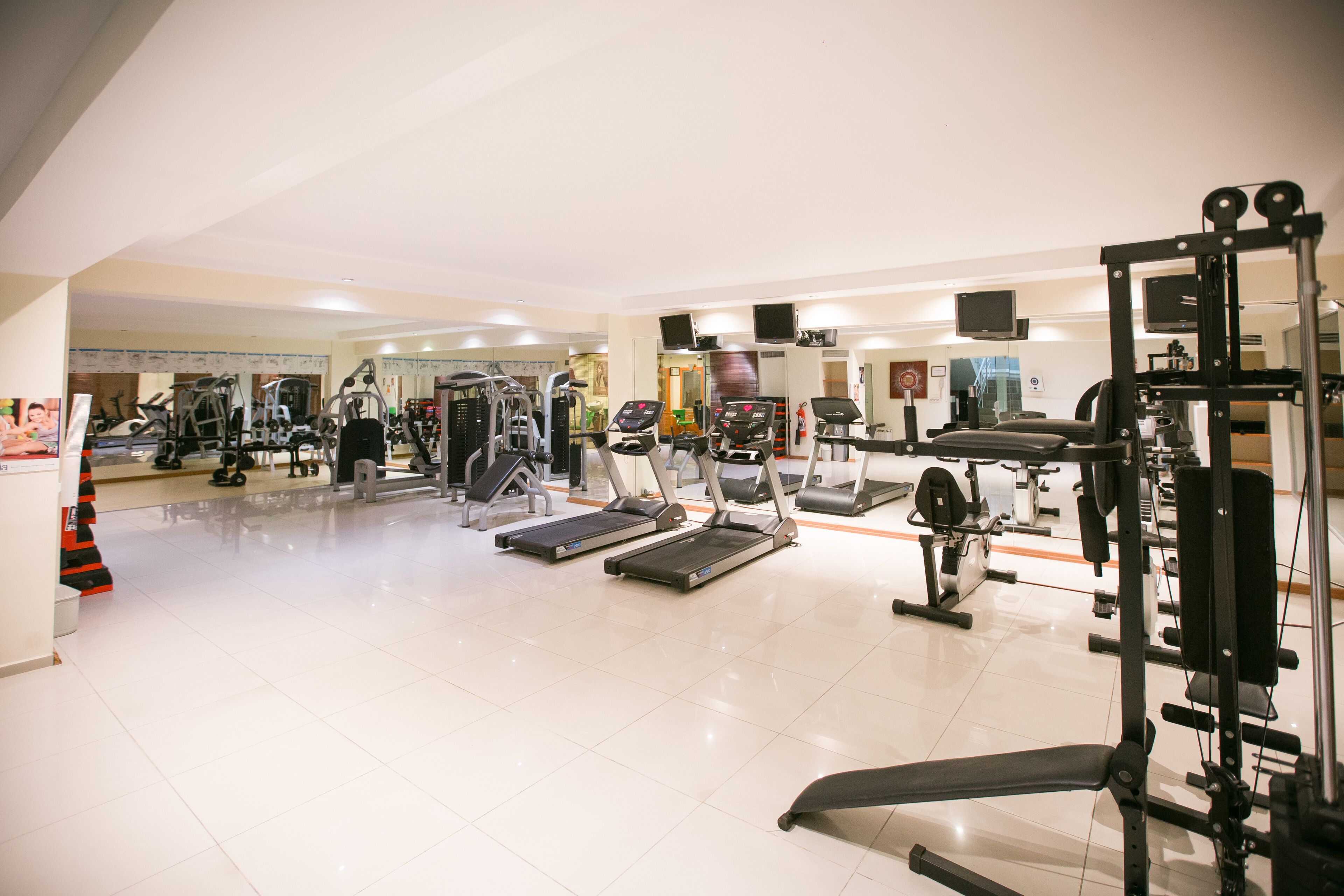 A gym with various exercise equipment including treadmills, weight machines, and a bench.