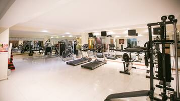 A gym with various exercise equipment including treadmills, weight machines, and a bench.