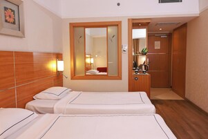 Ein Hotelzimmer mit zwei Betten, einem hölzernen Kopfteil, einem Spiegel, einem kleinen Schreibtisch mit Lampe und einer Tür zu einem Badezimmer.