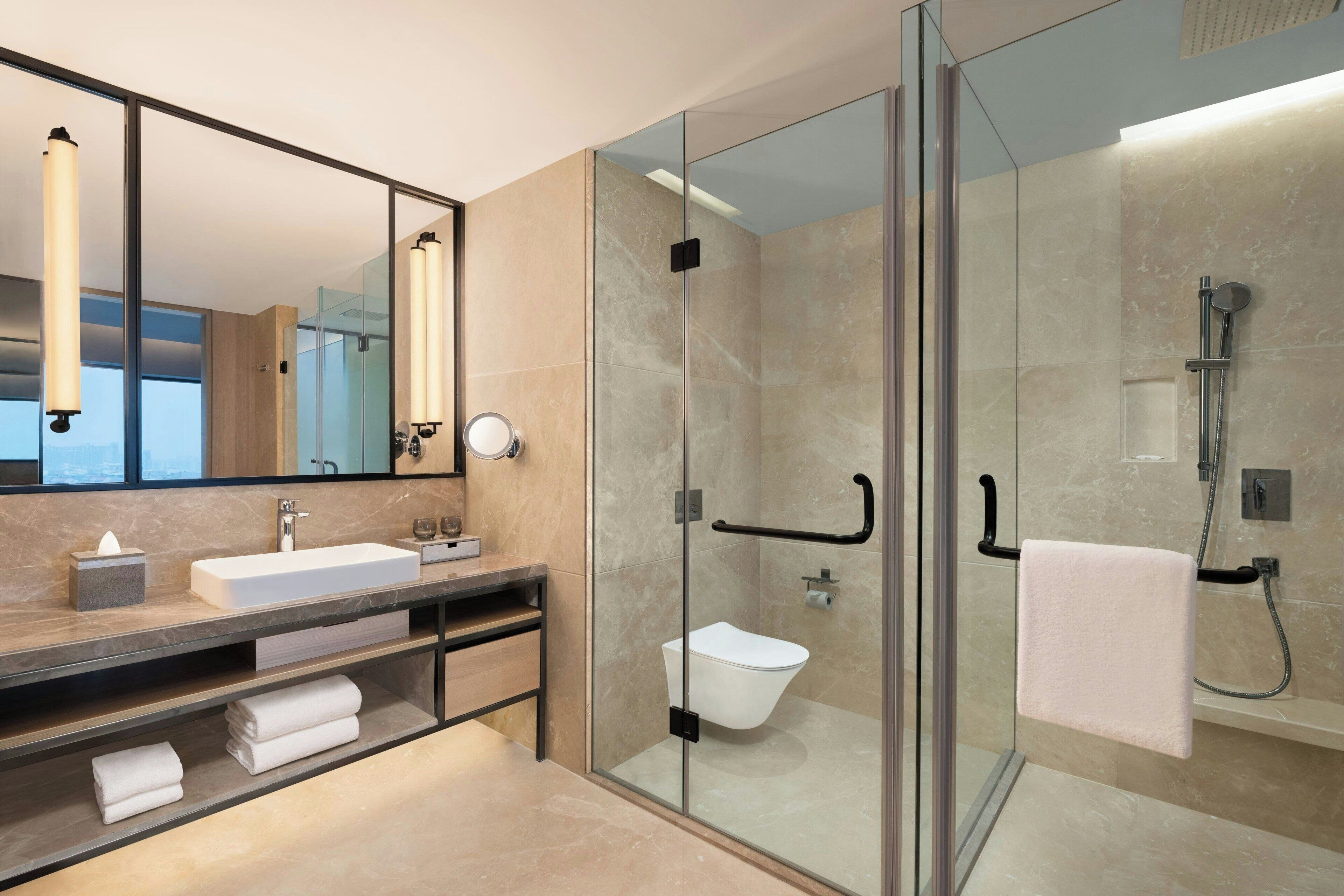 A modern bathroom with a glass-enclosed shower, a large mirror, and a vanity with a sink and towel storage.