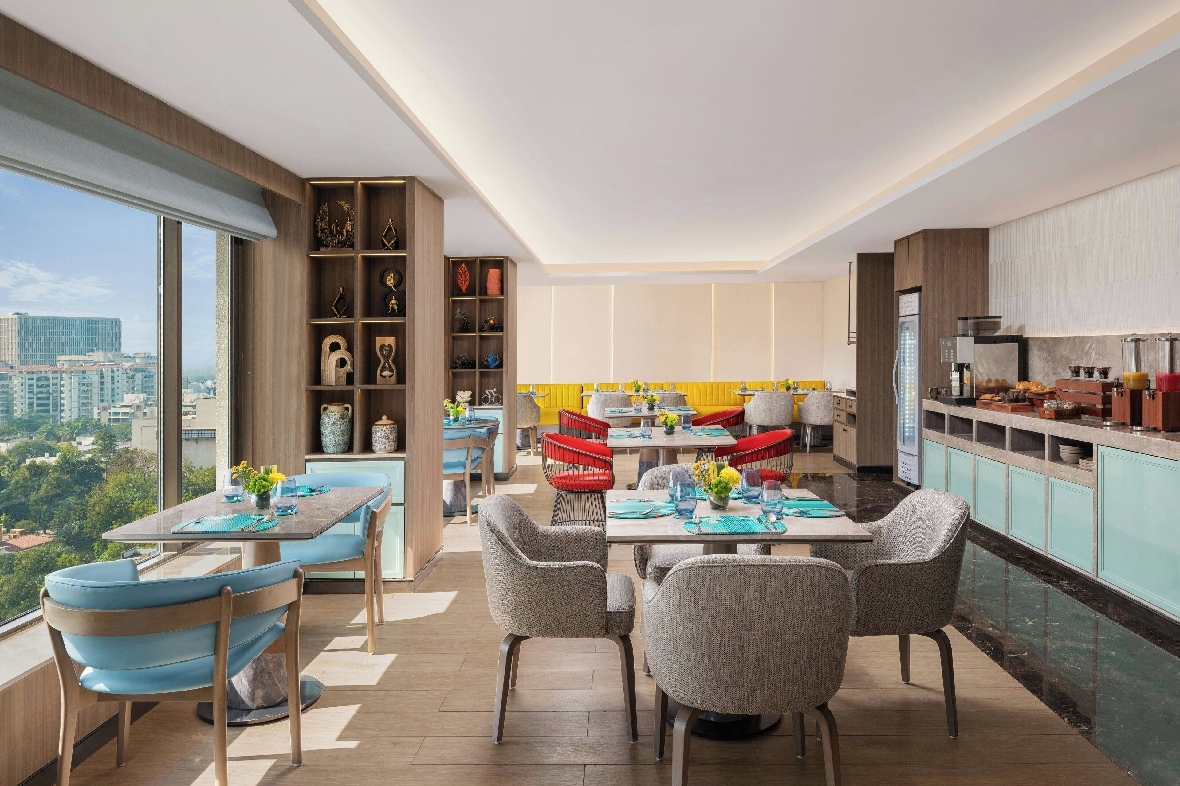 A modern dining area with a high ceiling, large windows, and a city view.