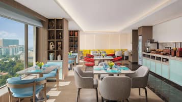 A modern dining area with a high ceiling, large windows, and a city view.