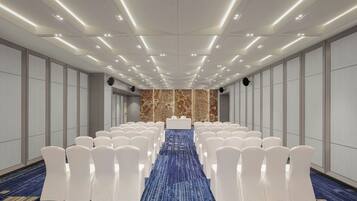 A conference room with rows of white chairs, a podium at the front, and a patterned carpet.