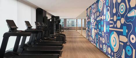 A gym with treadmills and exercise equipment, a wooden floor, and a colorful abstract wall.