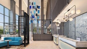 Een moderne hotellobby met een receptiebalie, een zithoek en grote ramen met uitzicht op de stad.