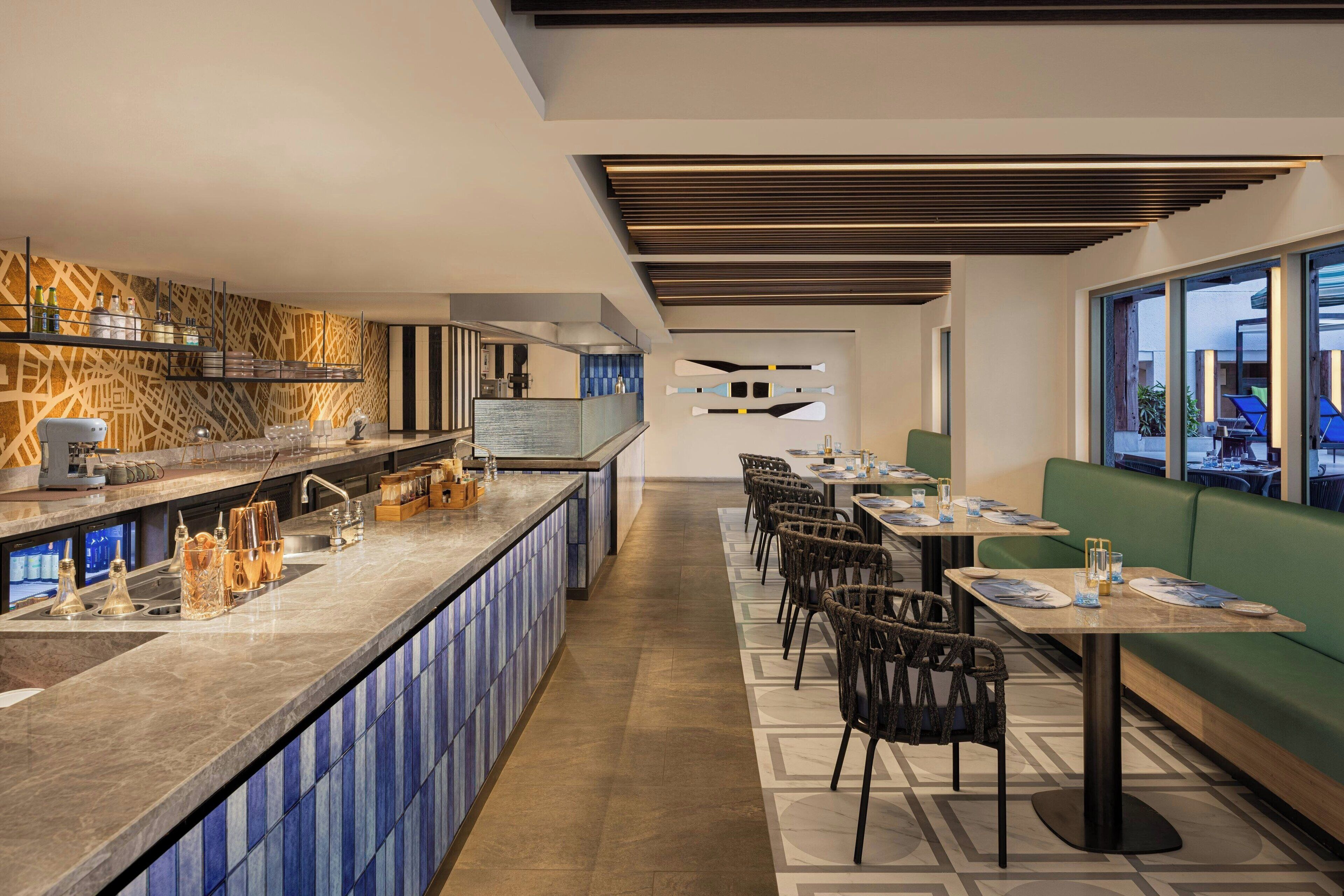 Un restaurante moderno con una barra alargada, zona de estar y grandes ventanales.