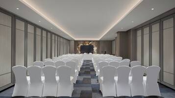 A conference room with rows of white chairs, a large screen at the front, and a patterned carpet.