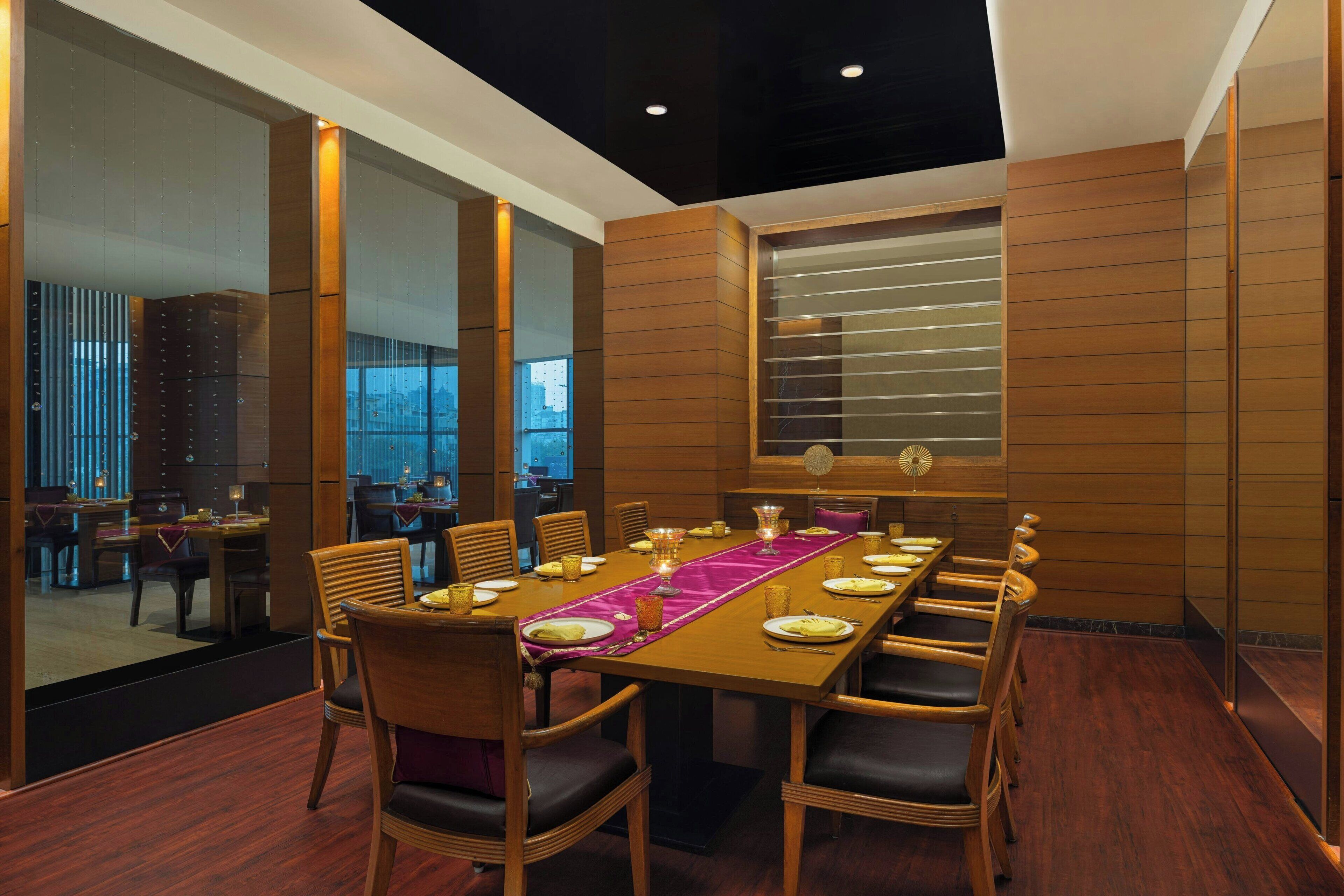 A modern dining area with a long table set for six, surrounded by wooden chairs with dark cushions.